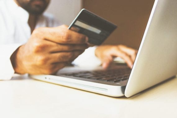 Image of a shopper holding a credit card by a laptop