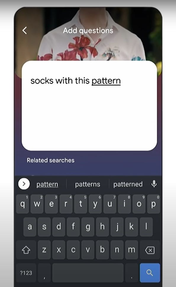 A smartphone screen with a text box overlaid on an image of a person wearing a colourfully patterned shirt. The text being input reads: socks with this pattern