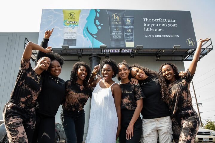 black business month - black girl sunscreen team in front of a promotional billboard